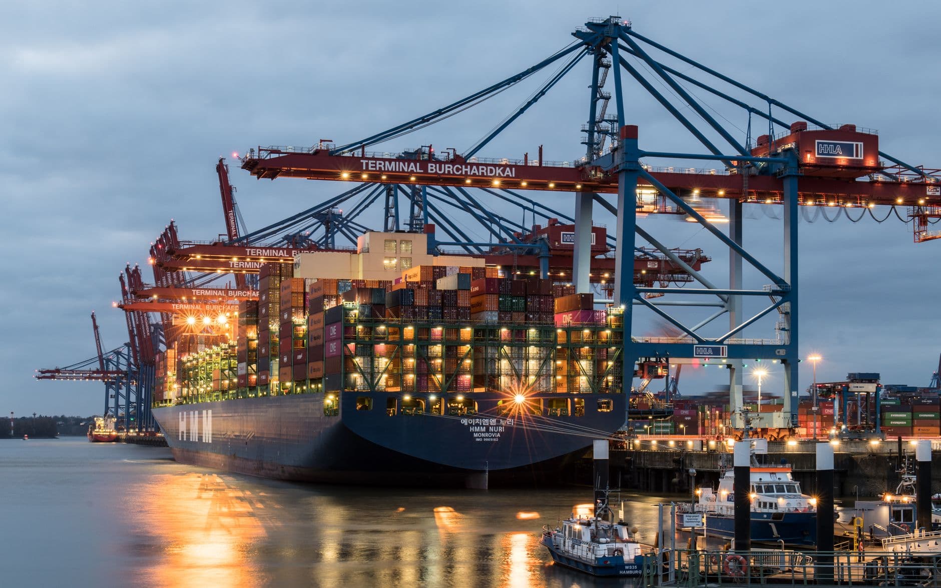 Container ships alongside at Terminal Burchardkai in Hamburg at dusk, the kind of multi-port fleet cloud crew management software has to keep in one record
